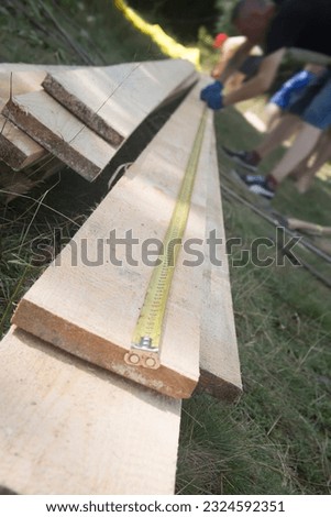 Yellow measuring tape on wooden plank. Construction industry, housework do it yourself. Construction worker using tape measurements to measure planks Royalty-Free Stock Photo #2324592351