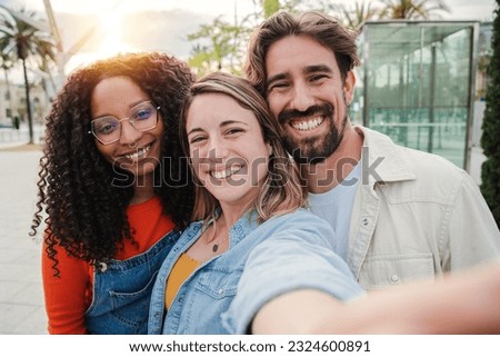 Three young adult friends smiling taking a selfie portrait and having fun together. Group of multiracial cheerful people celebrating their friendship. Two women and one man with positive expression Royalty-Free Stock Photo #2324600891