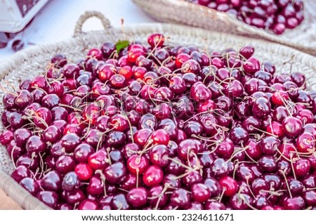 A bunch of cherries in a wicker basket in outdoors market. Close-up view in natural lights with selective focus on foreground and blur background  with dark periphery vignetting frame.