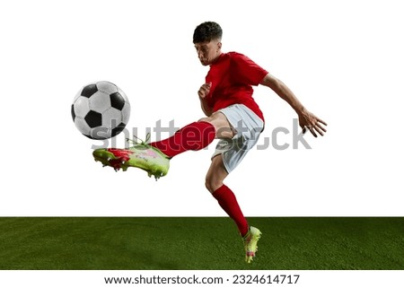 Competitive man, football player in red uniform training, kicking ball with leg against white background. Concentration. Professional sport, action, lifestyle, competition, hobby, training, ad concept