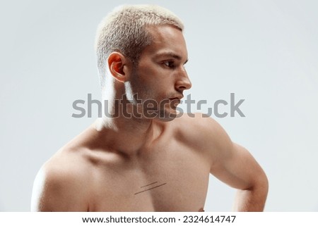 Close-up portrait of handsome young man with blonde hair, well-kept skin posing shirtless against grey studio background. Concept of male natural beauty, body care, health, sport, fashion, ad Royalty-Free Stock Photo #2324614747