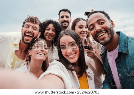 Big group of young adult happy friends smiling taking a selfie portrait and looking at camera with friendly expression. A lot of cheerful multiracial people celebrating and laughing. Buddies bonding