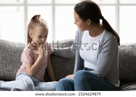 Serious mother talking to sad upset preschooler daughter kid at home. Mum consoling quiet girl, giving love, comfort, support, touching shoulder of child at home. Psychology, therapy, empathy concept