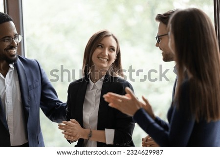 Laughing employees warmly welcoming young lady intern on workplace, friendly teammates congratulating woman coworker with promotion, partners praising businesswoman for creating successful project Royalty-Free Stock Photo #2324629987