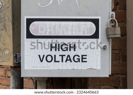 A securely locked utility box with High Voltage written on it and the word Danger faded from the sun