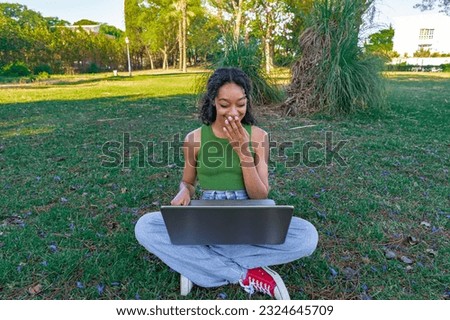 Girl using her pc sitting in the park in the shade, a sunny and hot summer day.
