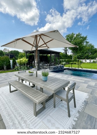 Gorgeous outdoor living backyard patio with pergola, outdoor rug,  tequila bar, dining set, couch, television, pool with waterfall , fire pit and stunning Techo Bloc patio pavers. Inspired by Tulum. Royalty-Free Stock Photo #2324687527