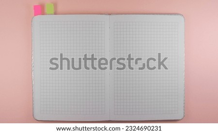 on a pink background lies a notebook in a cage with bookmarks