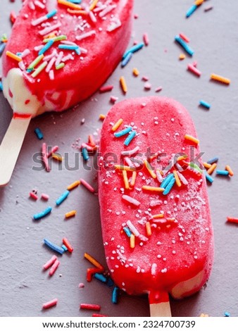 Strawberry ice cream lollies with sugar sprinkles, one with a bite taken out