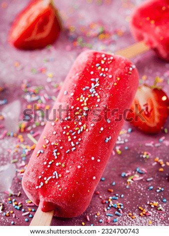 Strawberry ice cream lollies with sugar sprinkles, one with a bite taken out