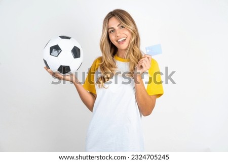 Photo portrait of Young beautiful woman holding football ball over white background  doing purchase with pointing finger credit bank card