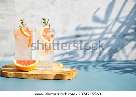 A chilled cocktail with fresh grapefruit slices and a sprig of rosemary under the shade of palm trees. Summer cold drinks. Soda with citrus Royalty-Free Stock Photo #2324715963