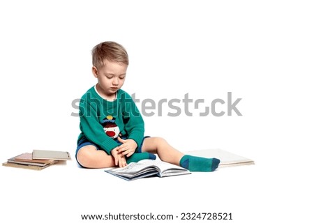A little boy, sitting on a shelf, examines with interest the pictures in the book that was read to him.The child is isolated on white. The concept of early childhood development