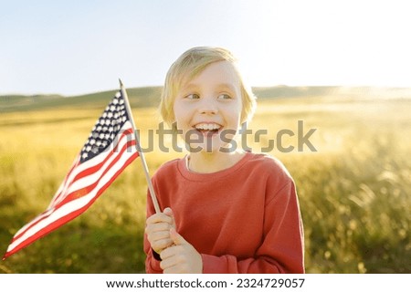 Cute little boy celebrating of July, 4 Independence Day of USA at sunny summer sunset. Child running with american flag of United States on wheat field. Proud little american boy holding country flag