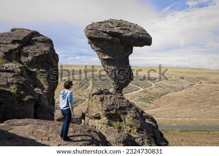 A young woman stands on a rock ledge looking at the famous Balanced Rock near Buhl, Idaho. Royalty-Free Stock Photo #2324730831