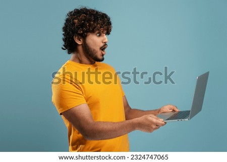 Portrait of excited Indian man using laptop, high speed internet, connection isolated on blue background. Attractive student holding computer preparing for exam, online shopping