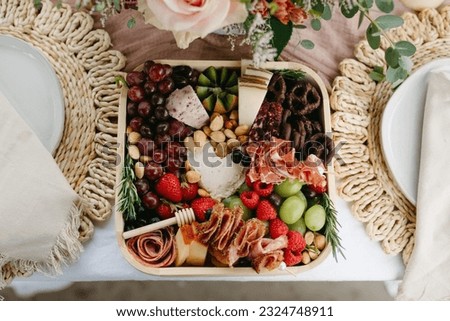 Detail of charcuterie fruits, cheeses, and nuts on a platter between two plates on a white table Royalty-Free Stock Photo #2324748911