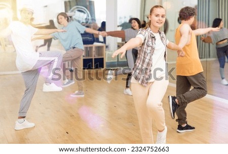 Interested modern teen girl practicing dynamic boogie-woogie in pair with boy during group class in dance studio for youth. Royalty-Free Stock Photo #2324752663