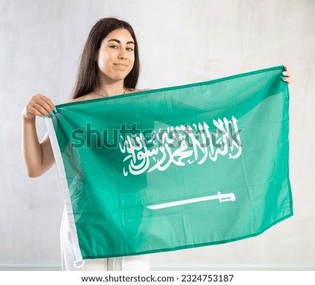 Young smiling brunette woman posing holding big Saudi Arabia flag in studio