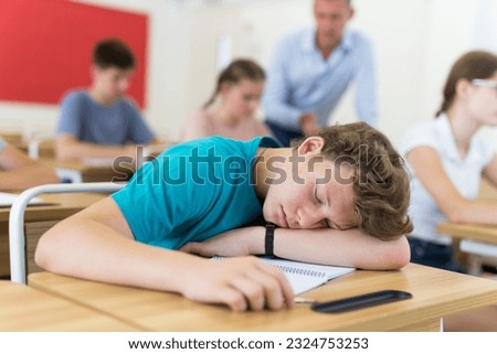 Teenager students sitting in class room and listening, but one boy sleeping on desk. Royalty-Free Stock Photo #2324753253
