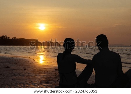 Couple in love watching the sunset together on beach travel summer holidays. People silhouette from behind sitting and enjoying the view sunset sea on a tropical destination vacation