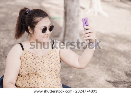 Woman wearing dark glasses smiling and taking selfie in the park.