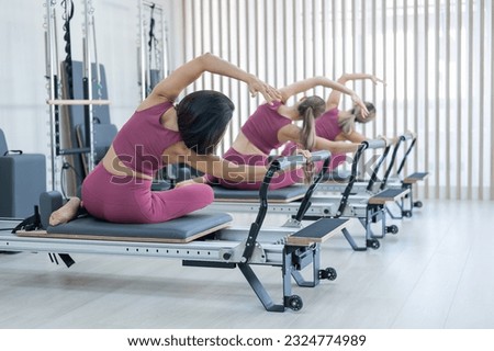 Three Asian women in pink sportswear doing side bends on a reformer machine. Pilates classes. Royalty-Free Stock Photo #2324774989