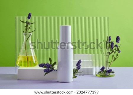 Front view of white bottle unbranded displayed on green background with lavender, white podiums and acrylic sheet. Lavender oil could be a gentle way to treat acne due to its ability to kill bacteria. Royalty-Free Stock Photo #2324777199