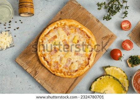 Top view shot of delicious tasty juicy of Hawaiian traditional Italian crust thin crispy ham and pineapple pizza placed on wooden cutting board with ingredients sliced tomatoes, ketchup and salt.