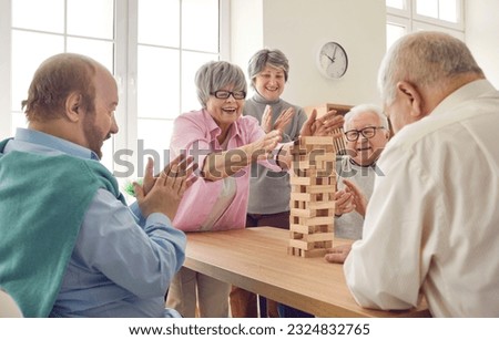 Group of happy senior people having fun and playing board games in retirement home. Several cheerful old men and women gather around table and take turns to take wood blocks out of wooden tower Royalty-Free Stock Photo #2324832765