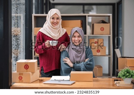 A happy young Asian Muslim female online seller working with her employee in the office. SME business, online shop owner