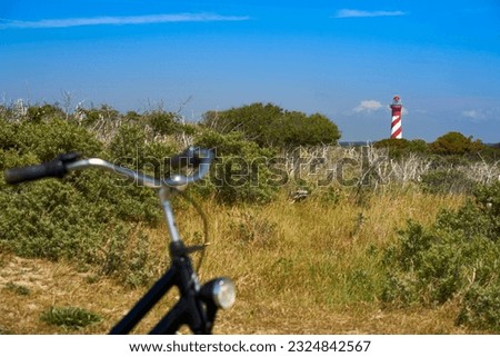 Dutch lighthouse on the horizon. Handlebar of bicycle out of focus. Landscape shot on a sunny bright vacation afternoon. Blue sky for copy space. Holland, Zeeland, Haamstede.
