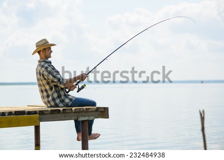 Side view of young man sitting on pier with rod