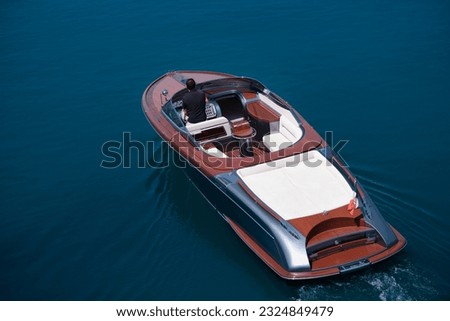 Luxurious big boat for millionaires slow motion on dark blue water top view. Fashion wooden boat with a man moving on the water aerial view. Luxury boat with white leather chairs move on the water. Royalty-Free Stock Photo #2324849479