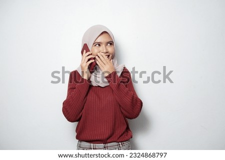 Beautiful smiling happy Asian girl wearing hijab talking on mobile phone with friend, looking at empty space