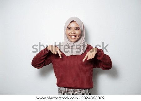 Portrait of Asian Muslim woman smiling pointing fingers down, inviting customers to special event isolated over white background