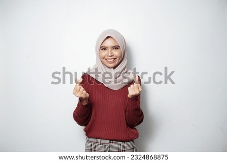 Beautiful smiling Asian woman in red sweater showing Korean heart with two fingers crossed, express joy and positivity isolated over white background