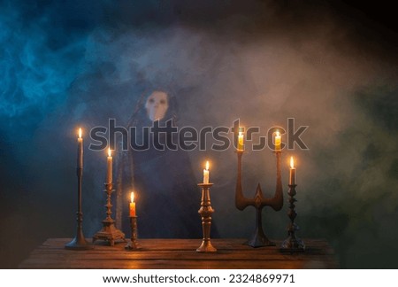 Grim reaper with burning candles on wooden table in the dark background