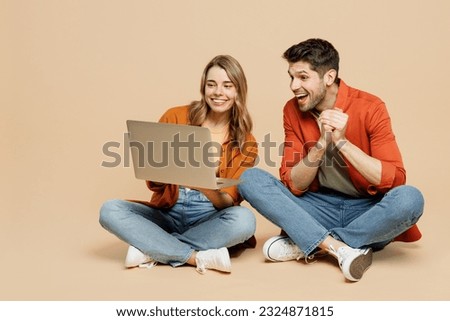 Full body excited young couple two friends family IT man woman wearing casual clothes together sitting hold use work on laptop pc computer isolated on pastel plain light beige color background studio Royalty-Free Stock Photo #2324871815