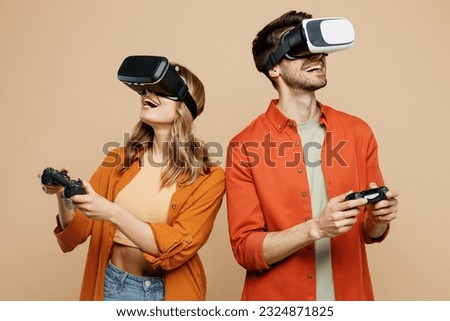Young couple two friends family man woman wear casual clothes together watching in vr headset pc gadget hold in hand play pc game with joystick console isolated on pastel plain beige color background