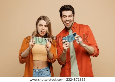 Young couple two friend family man woman wear casual clothes use play racing app on mobile cell phone hold gadget smartphone for pc video games together isolated on pastel plain light beige background
