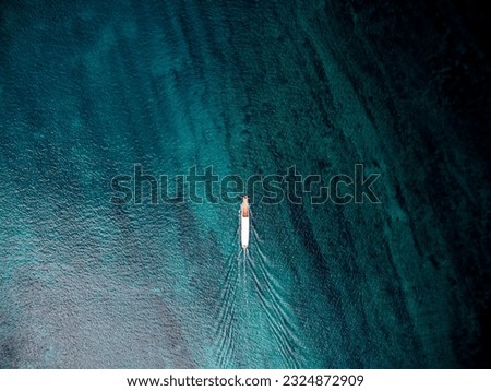 top down drone shot of boat moving forward showing trail on the water and sea bed is visible