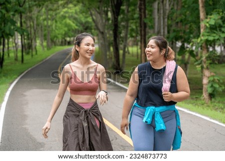Two young women, skinny and overweight, enjoy each other's company during their morning walk at a running track of a local park Royalty-Free Stock Photo #2324873773