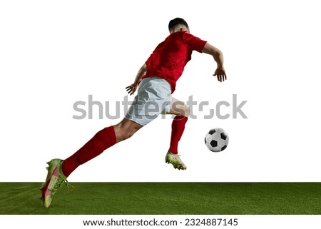 Bottom view dynamic image of young man in red uniform, football player in motion running with ball on field against white background. Concept of professional sport, action, competition, training, ad Royalty-Free Stock Photo #2324887145
