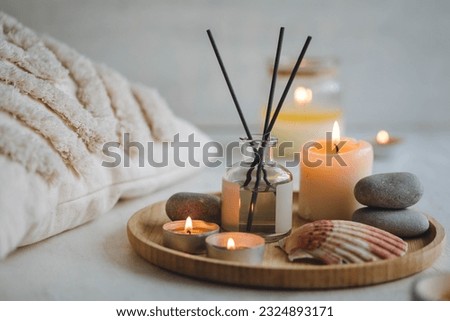 Burning candles on bamboo tray, cozy home atmosphere. Relaxation, detention zone in the living or bedroom. Stones, sea shells as decor. Apartment natural aroma diffusor with ocean breeze fragrance.  Royalty-Free Stock Photo #2324893171