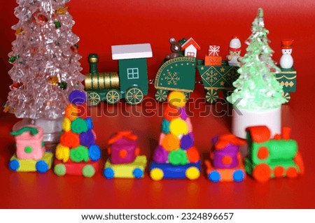 A toy Christmas train made of plasticine with gifts and Christmas trees. Bright red background. New Year decorations.