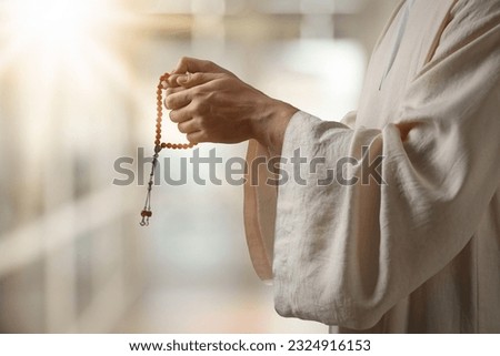 Muslim man with misbaha praying on blurred background, closeup Royalty-Free Stock Photo #2324916153