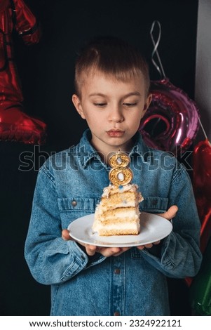 Children's birthday celebration. A joyful boy, a schoolboy, with a piece of cake and a candle in the shape of the number eight. Boy blowing out the candles on the cake. Front view