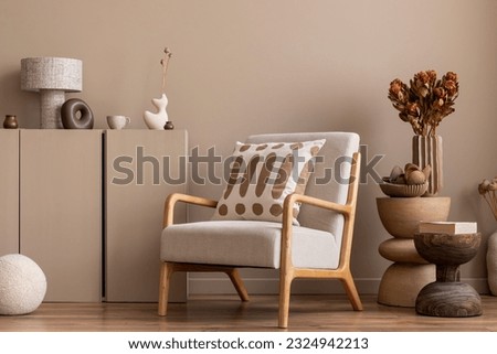 Cozy composition of living room interior with gray armchair, dark pillow, beige sideboard, wooden coffee table, vase with branch, round pillow and personal accessories. Home decor. Template.