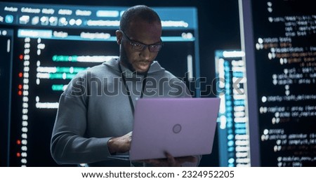 Portrait of Professional Programmer Developing a Big Data Interface Software Project.Young Black Man Working on Laptop Computer, Looking at Big Digital Screen Displaying Back-end Code Lines Royalty-Free Stock Photo #2324952205